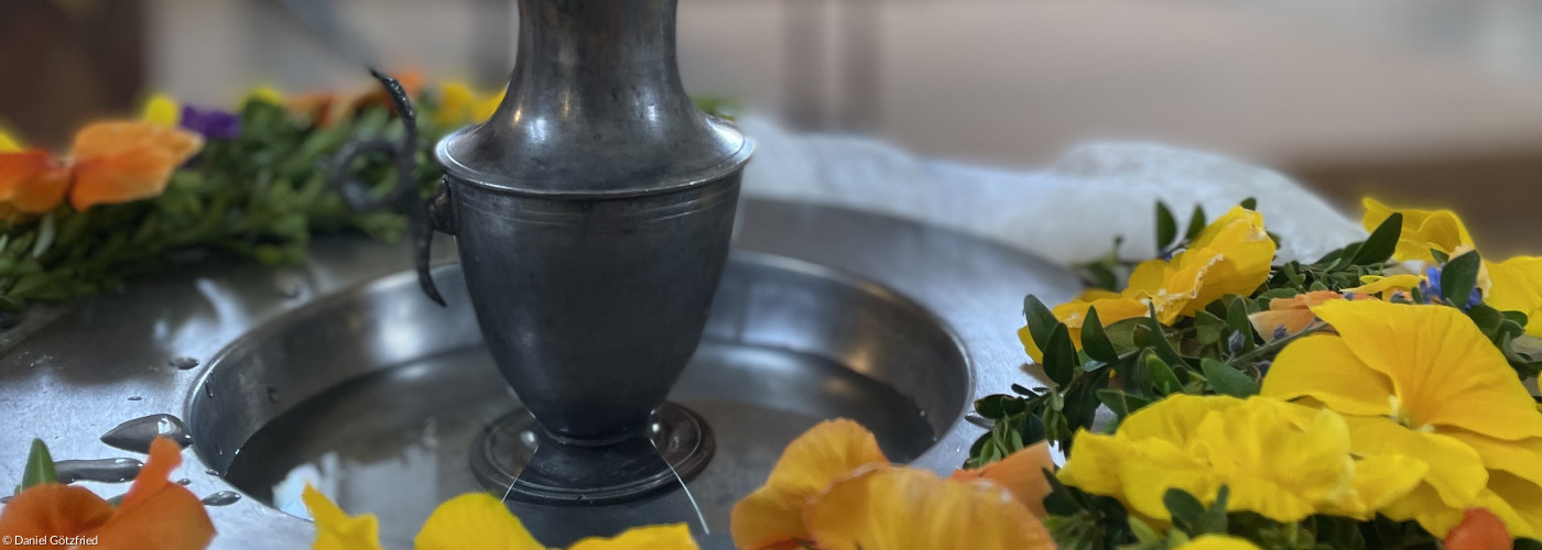 Taufstein mit Blumenkranz und Wasserkrug